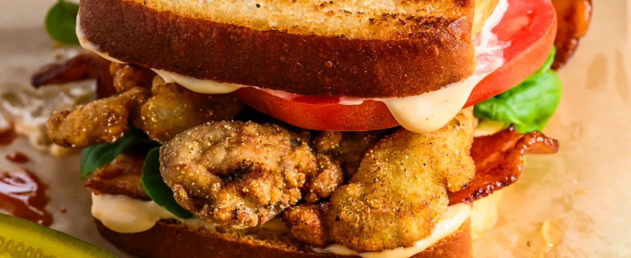 A fried oyster sandwich with bacon, tomato and mayonnaise on toasted bread
