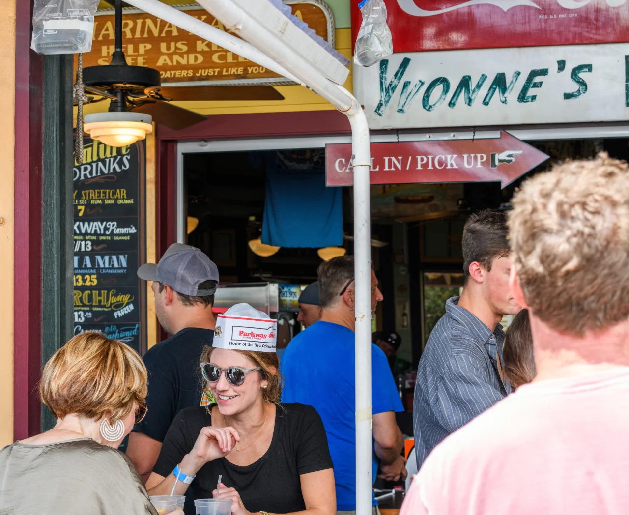 A smiling woman in a Parkway paper hat at a crowded festival table