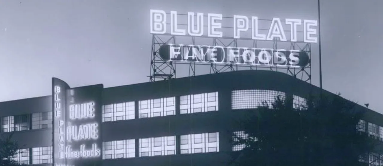 The Blue Plate Fine Foods building in New Orleans at night, its neon sign lit